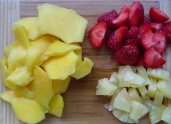 Chopped up pieces of mango, pineapple and strawberries on a wooden board