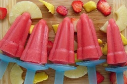 red ice lollies displayed on a wooden board surrounded by pieces of mango, pineapple and strawberries